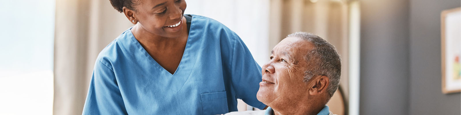 A female senior living nursing assistant smiling at a male resident sitting in a wheelchair