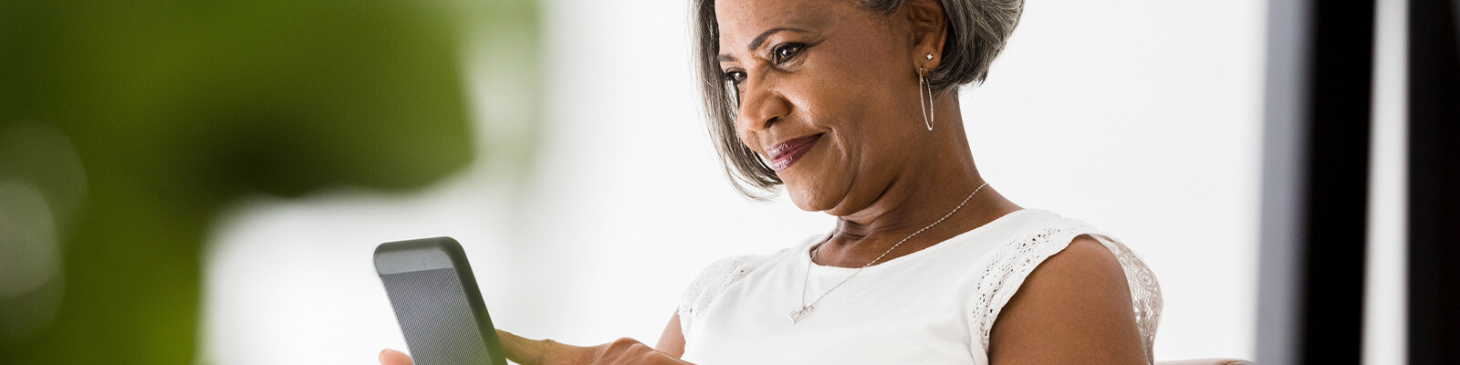 A senior female in a white shirt looking down at a smartphone and smiling