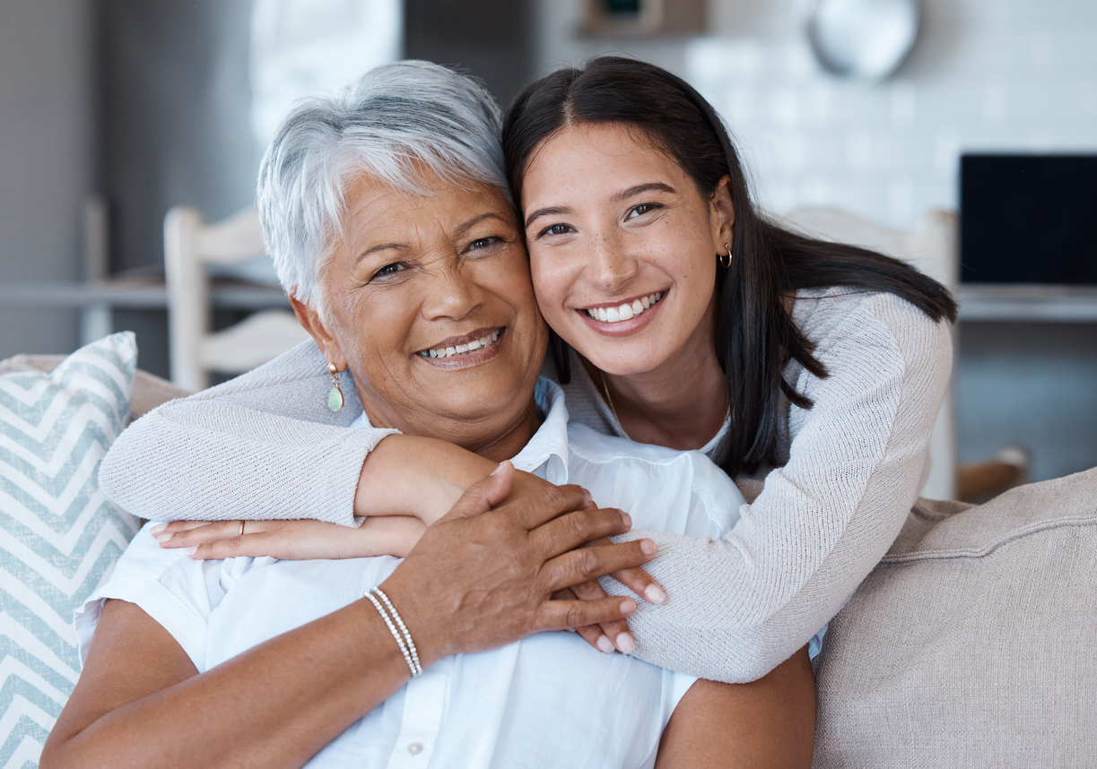 An adult daughter leans in to hug her mother, a memory care resident at Traditions. Quincy Place Senior Living.