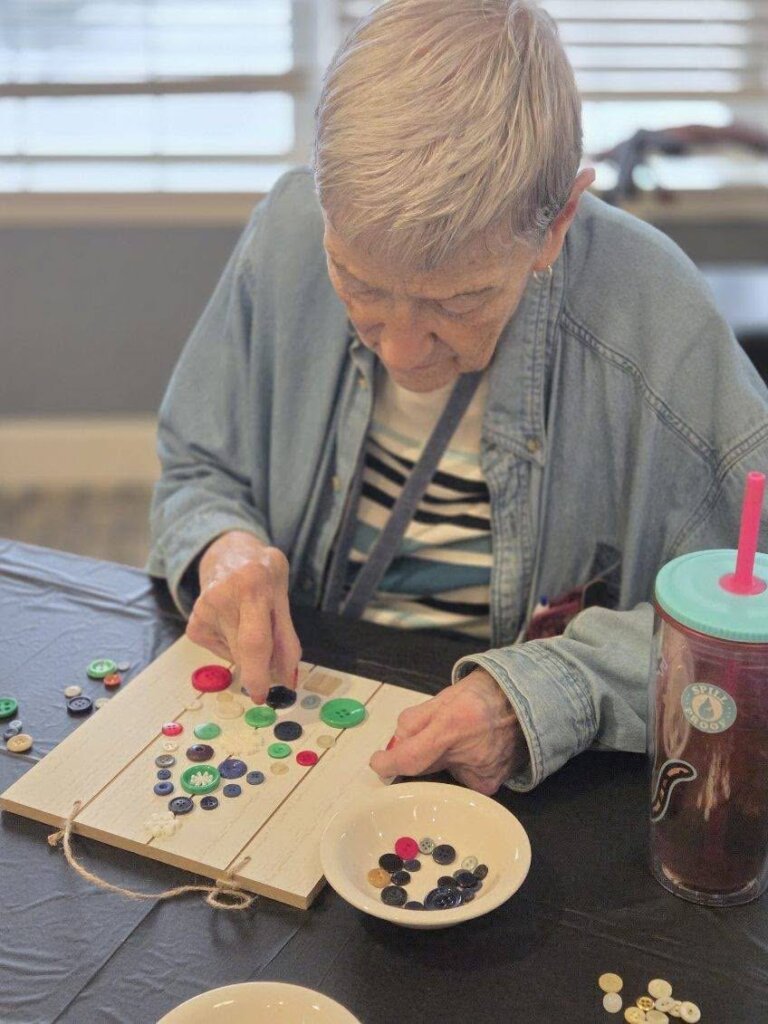 Quincy Place resident arranging colorful buttons on a wooden craft board during an activity session