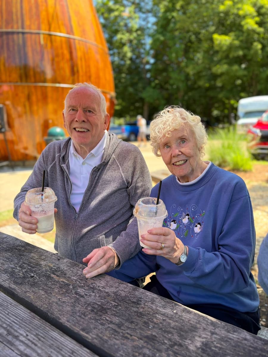 Two smiling residents holding root beer floats at an outdoor picnic table during a group outing